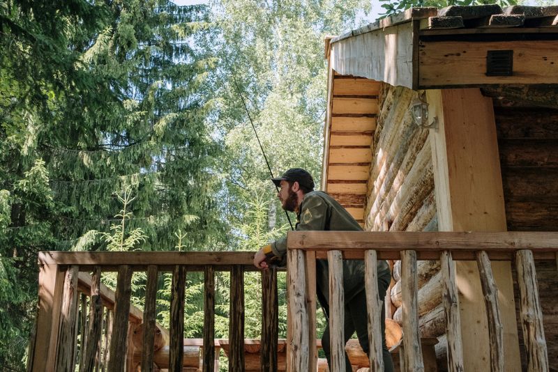 A Man Standing On A Cabin House' Verandah Looking Into The Forest